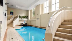 Una piscina interior con una escalera curva y vistas al cielo a través de amplios ventanales.