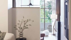 Un dormitorio moderno con una cama, un jarrón con ramas, una lámpara de pie y vistas al exterior.