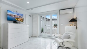 A modern living room with a flat-screen TV, a white sofa, a massage chair, and a sliding glass door leading to an outdoor area. - Upscale Studio in Kirribilli with private Terrace (Kirribilli)