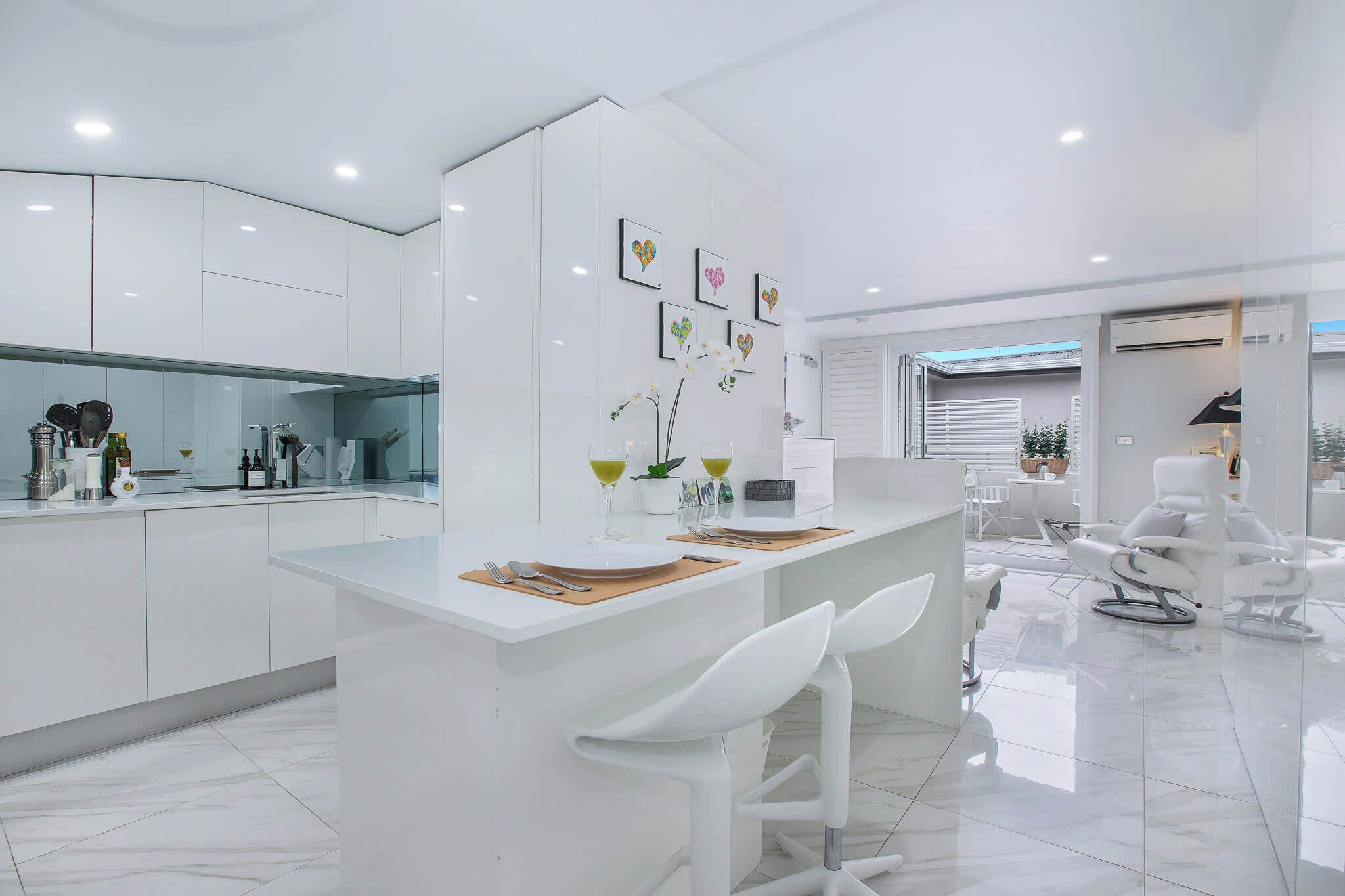 A modern kitchen with white cabinetry, a central island with bar seating, and a dining area with white chairs.