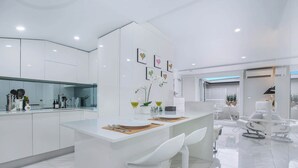 A modern kitchen with white cabinetry, a central island with bar seating, and a dining area with white chairs. - Upscale Studio in Kirribilli with private Terrace (Kirribilli)