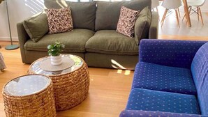 Ein modernes Wohnzimmer mit einer Couch, einem blauen Sessel und zwei Korbstühlen.