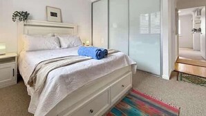 Ein Schlafzimmer mit einem Bett, Nachttischen, einem kleinen Tisch, einem blauen Handtuch, einem farbenfrohen Teppich und einem Schiebetürenschrank.