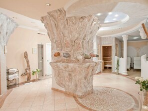 Ein Wellnessbereich mit großem Felsen als Mittelpunkt, einer Rezeption und einem runden Mosaikboden.