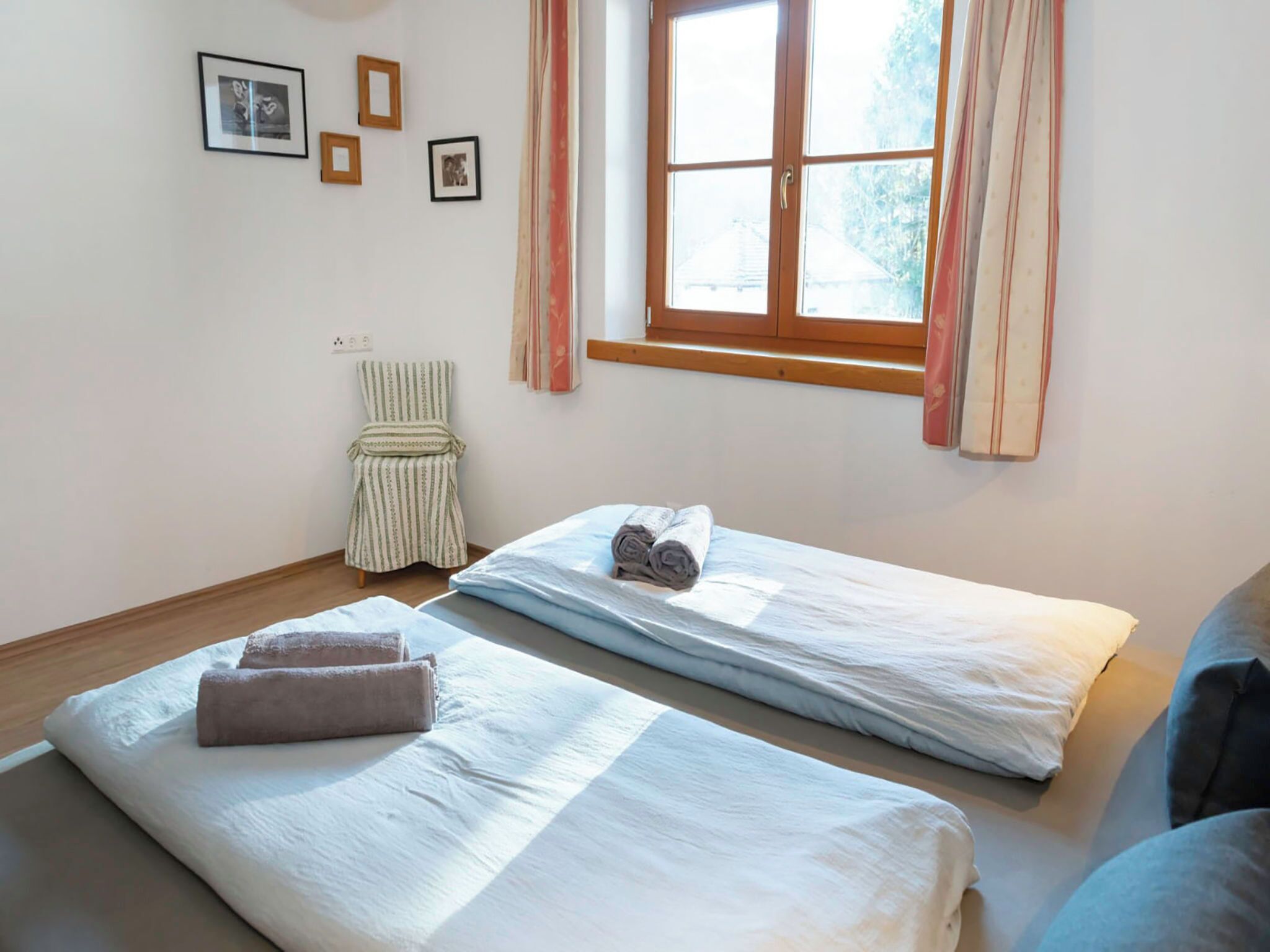 Ein Zimmer mit zwei Betten, einem Sessel und einem Fenster mit Vorhängen.