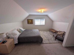 Ein kleines, gut beleuchtetes Schlafzimmer im Dachgeschoss mit einem Bett, einem Nachttisch, einem Schreibtisch und einem Fenster.