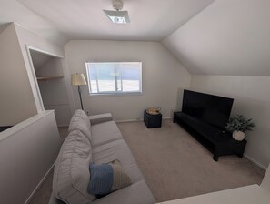 Ein Wohnzimmer mit einer Couch, einem Fernseher, einer Lampe, einem Fenster und einem Deckenventilator.