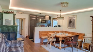 Ein gemütliches Wohnzimmer mit Kamin, eine Essecke mit Holztisch und Stühlen sowie eine Küche mit modernen Geräten.