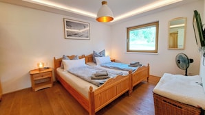 Ein Schlafzimmer mit zwei Holzbetten, einem Nachttisch mit Lampe, einem Fenster mit Aussicht, einem Spiegel und einem Standventilator.