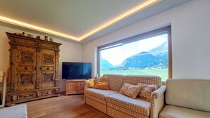 Una sala de estar con un sofá, un televisor, un mueble de madera y un ventanal con vistas a la montaña.