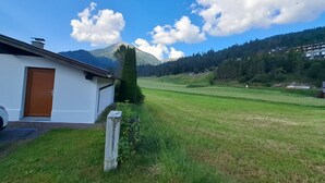 A white building with a brown door, a grassy field, and a mountain in the background. - Panorama by Interhome (Achenkirch)