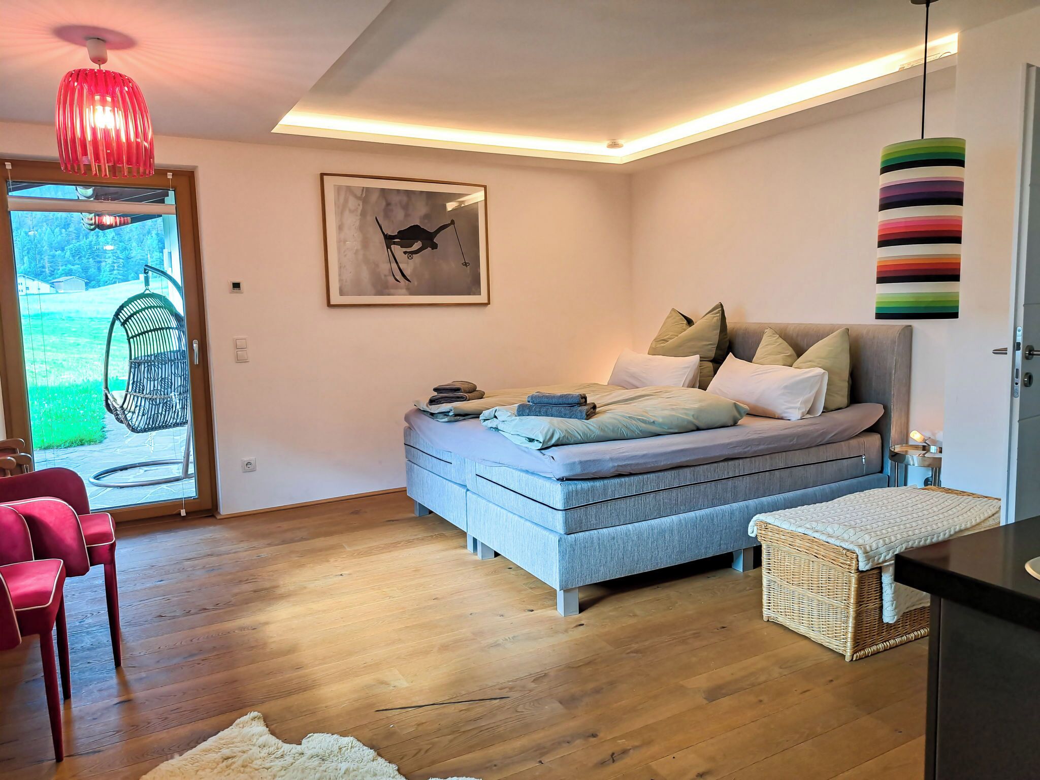 Een moderne slaapkamer met een bed, een hangstoel, een rieten mand en een rode hanglamp.