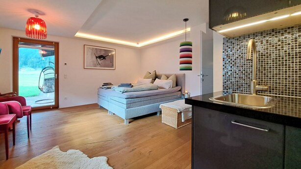 A modern bedroom with a bed, a small bedside table, a hanging light fixture, and a view of the outdoors. - Panorama by Interhome (Achenkirch)