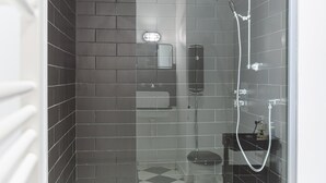 Eine gläserne Dusche mit gefliesten Wänden, einer sichtbaren Toilette und einer kleinen Ablage für Toilettenartikel.