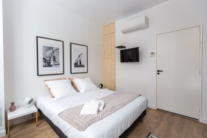 A bedroom with a bed, two framed pictures, a TV, and an air conditioning unit. - Charming AC studio in Bordeaux (Bordeaux)