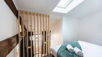 Une chambre avec un puits de lumière, un lit recouvert d’une couverture turquoise et un escalier en bois.