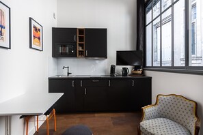 A modern kitchen with black cabinets, a microwave, and a coffee maker. There is a window with a view of buildings, a white table, and a patterned chair. - Modern AC duplex in the heart of Bordeaux (Bordeaux)