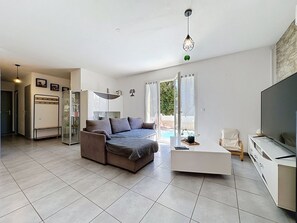 A modern living room with a sofa, a TV, a coffee table, and a sliding glass door leading to a pool. - Villa des Amoureux by Interhome (Saint-Geniès-de-Malgoirès)