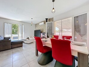 A modern living room with a dining area, large windows, and a stone accent wall. - Villa des Amoureux by Interhome (Saint-Geniès-de-Malgoirès)