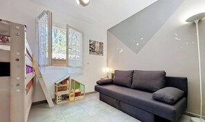Kompakti oleskelutila, jossa on sohva, pieni puinen leikkimökki ja ikkuna, jossa on verhot.