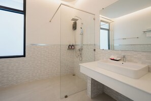 Un baño moderno con ducha de vidrio, un lavamanos blanco y un espejo grande.
