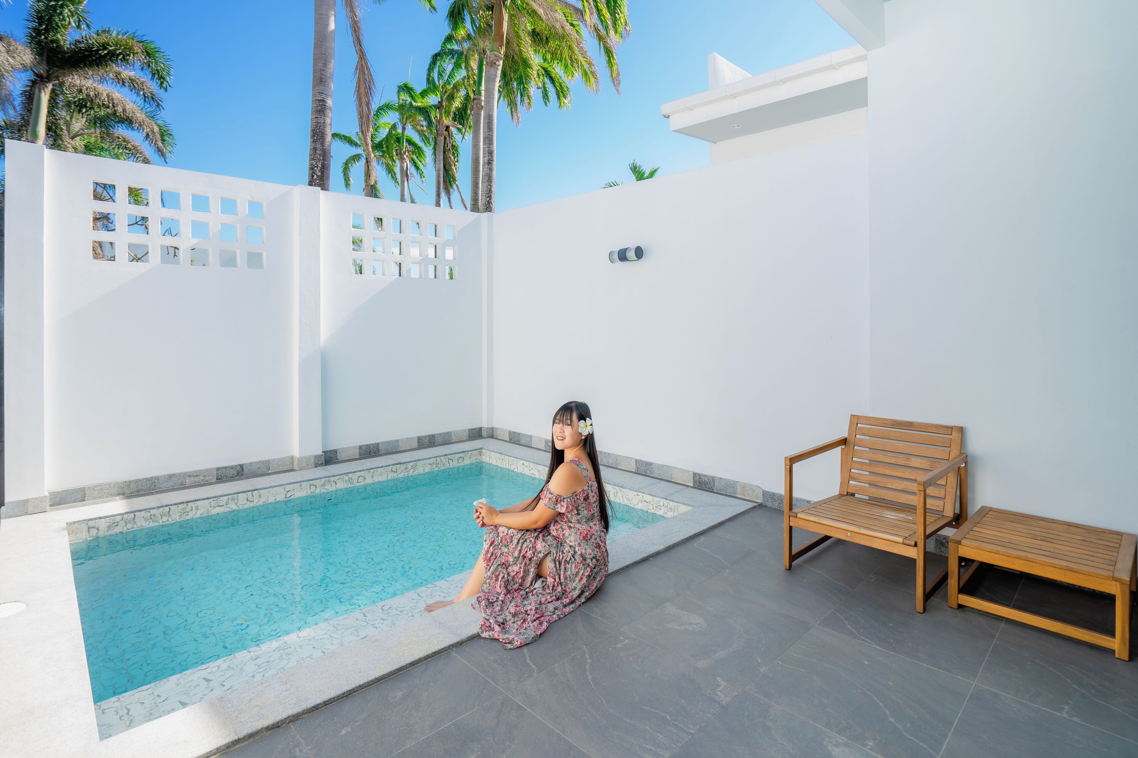 Un área de piscina con un banco de madera y una persona sentada junto a la piscina.