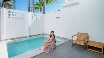 Un área de piscina con un banco de madera y una persona sentada junto a la piscina.