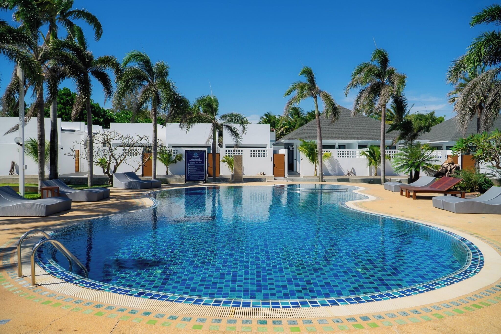 A swimming pool with lounge chairs, palm trees, and a building with a blue door.