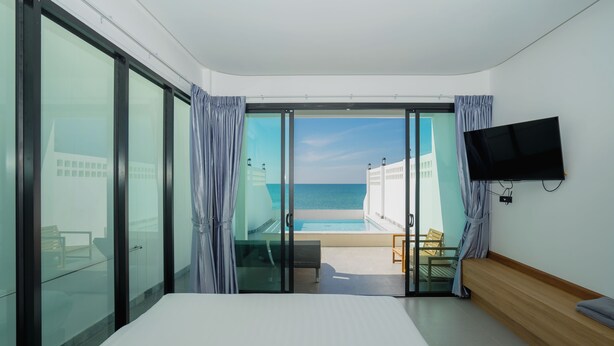 Habitación de hotel con cama, televisión, puerta corrediza de vidrio que da a un balcón con vista a la piscina y la playa.