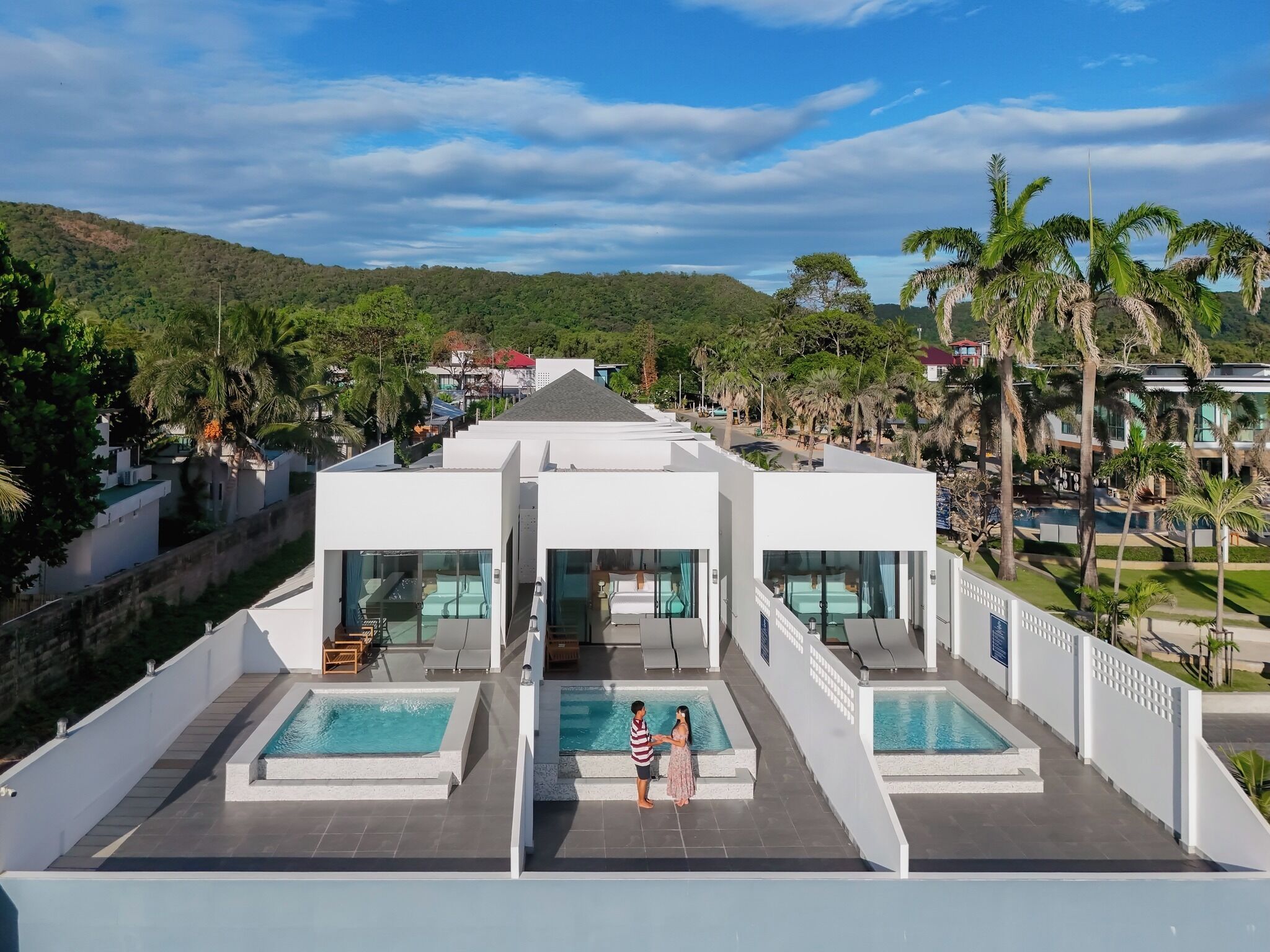 A modern hotel with a rooftop pool area, multiple guest rooms, and a view of the surrounding greenery and hills.