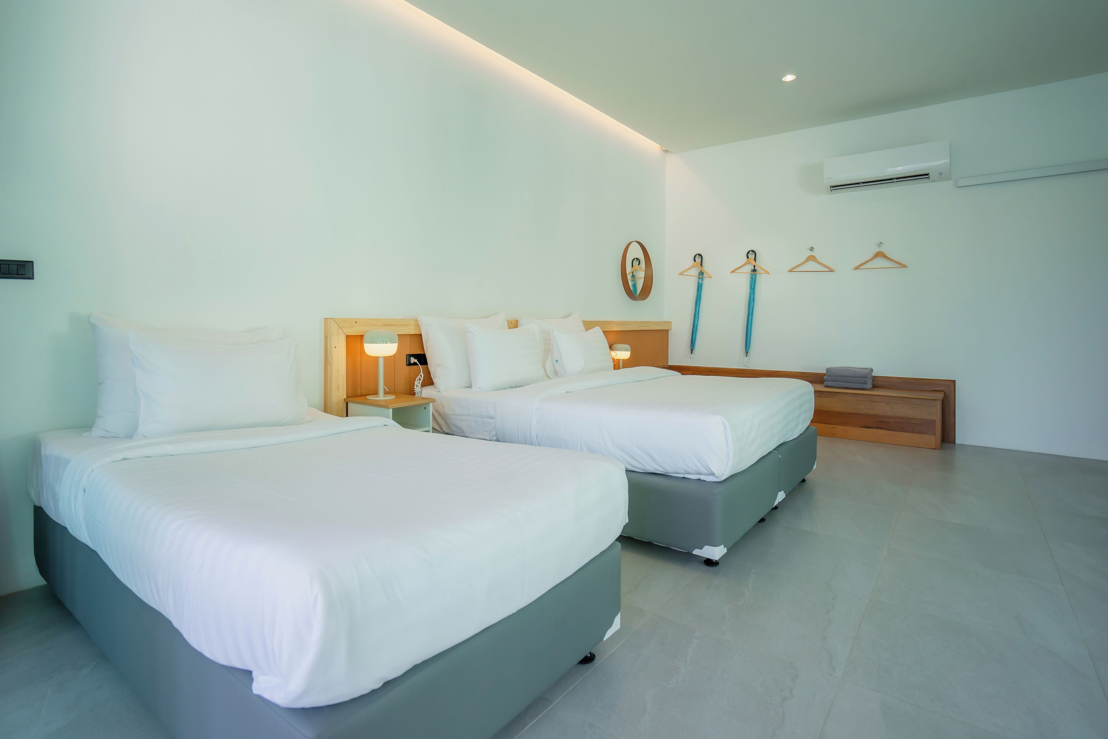 Habitación de hotel con dos camas, mesitas de noche, aire acondicionado instalado en la pared y un perchero con colgadores.