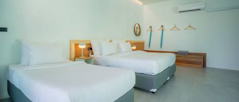 Habitación de hotel con dos camas, mesitas de noche, aire acondicionado instalado en la pared y un perchero con colgadores.