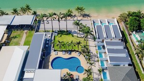 Vista aérea de un complejo turístico con una piscina central, varias habitaciones de huéspedes y una playa.