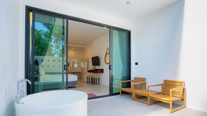 Un baño moderno con una bañera grande, zona de ducha con mampara de vidrio y un espacio de descanso con dos sillas de madera.