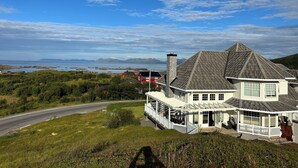 Una casa con un porche grande, vista al mar y una carretera en primer plano.