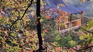 Un paysage montagneux avec une structure en bois, peut-être une cabane ou un poste d’observation, entouré d’arbres aux feuilles d’automne.