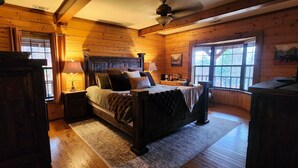 Une chambre dans une cabane en bois, avec un lit, des tables de chevet, une lampe, une fenêtre et un ventilateur de plafond.