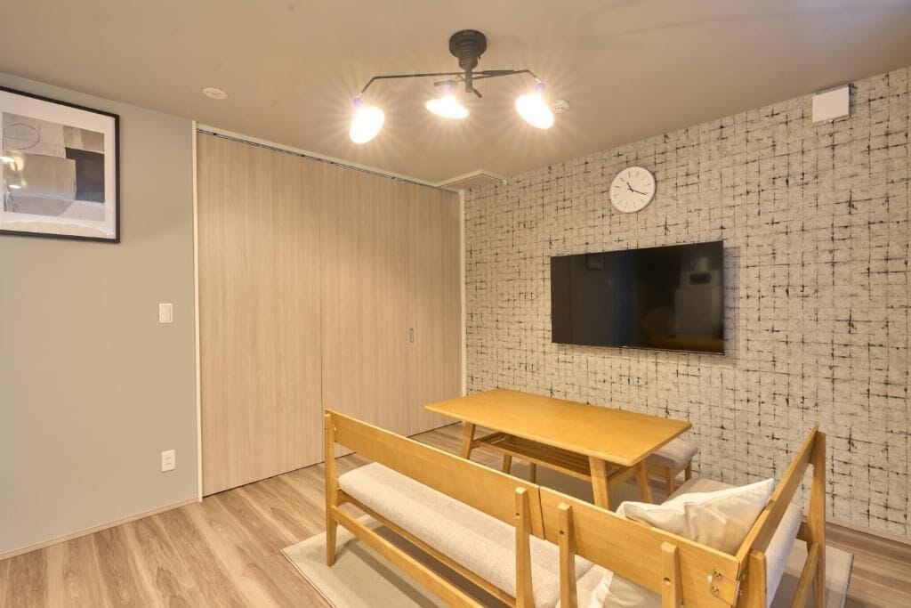 A room with a wooden table and bench, a TV mounted on the wall, and a clock.