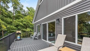 A deck with outdoor furniture, a grill, and a view of the surrounding trees.