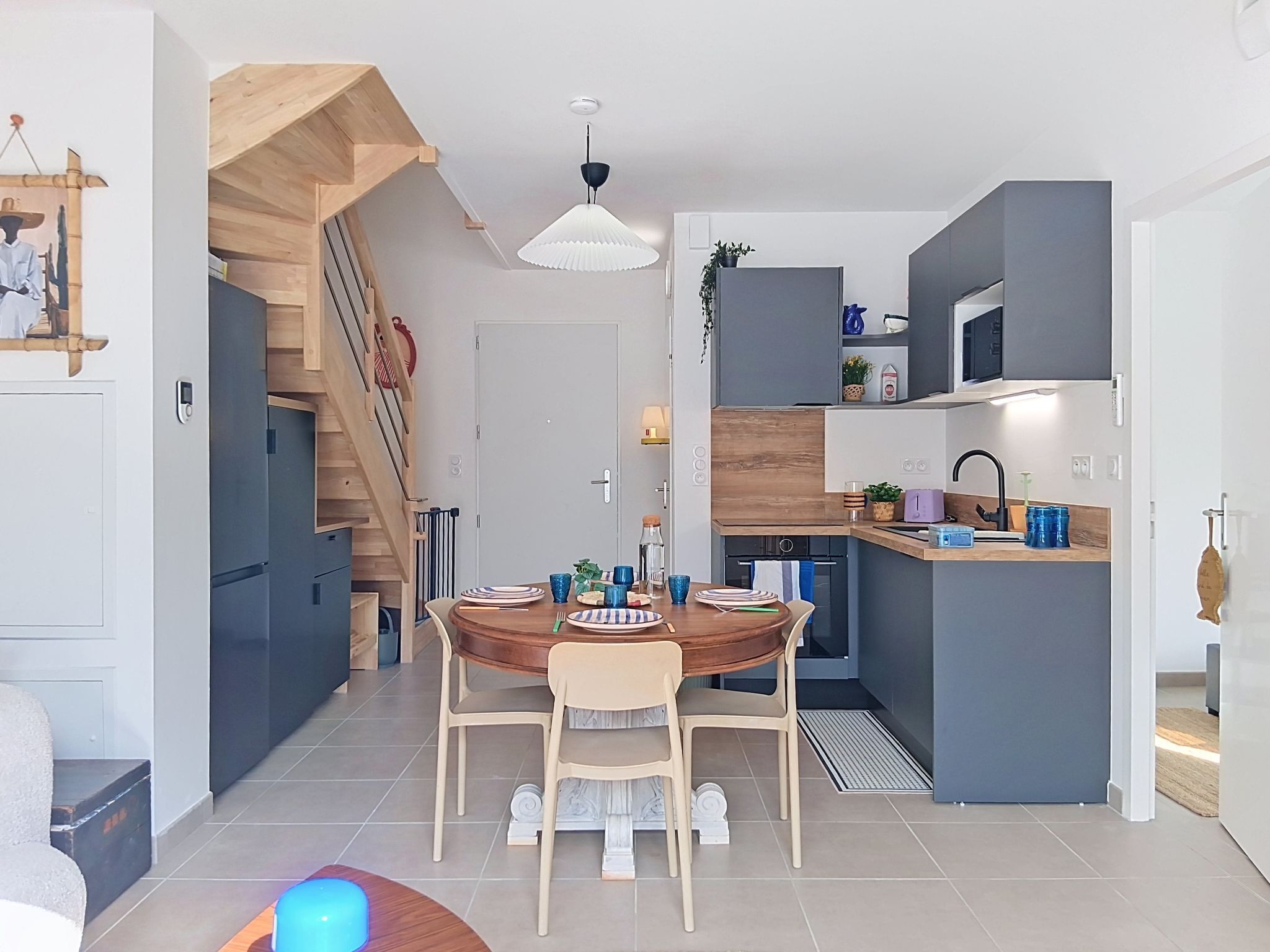 Eine moderne Küche mit einer zentralen Kochinsel, ein Essbereich mit Holztisch und -stühlen sowie eine Treppe, die in ein Obergeschoss führt.
