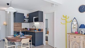 Moderni keittiö, jossa on tummat kaapit, keskellä sijaitseva keittiösaareke sekä ruokailutila, jossa on puinen pöytä ja tuolit.