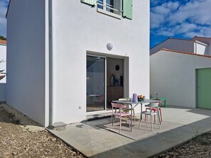 Un edificio moderno con un patio que incluye una mesa, sillas, un cerramiento de vidrio corredero y una puerta verde.