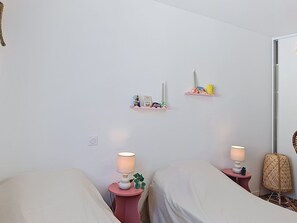 Ein Schlafzimmer mit zwei Betten, Nachttischen mit Lampen und Wandregalen mit Dekoration.