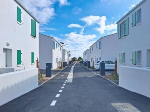 Eine Straße gesäumt von weißen Gebäuden, jedes mit grünen Fensterläden, und ein geparktes Auto auf der rechten Seite.