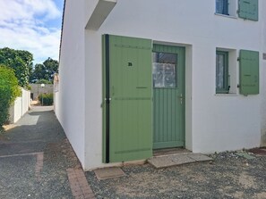 Ein weißes Gebäude mit grüner Tür, Hausnummer 26, und einem kleinen Fenster mit Vorhang.