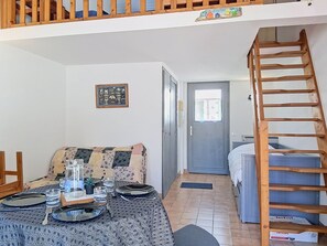 Ein möbliertes Zimmer mit einer Couch, einem Esstisch und einer Treppe sowie einer Tür zu einem weiteren Raum.