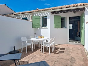 Eine Terrasse mit Tisch und Stühlen, ein kleiner Tisch mit einem Sessel und eine Tür zu einem Raum.