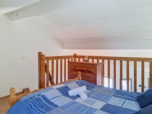 Ein Schlafzimmer mit einem Holzbettgestell, einer kleinen Holzkommode und einem Fenster mit Blick.