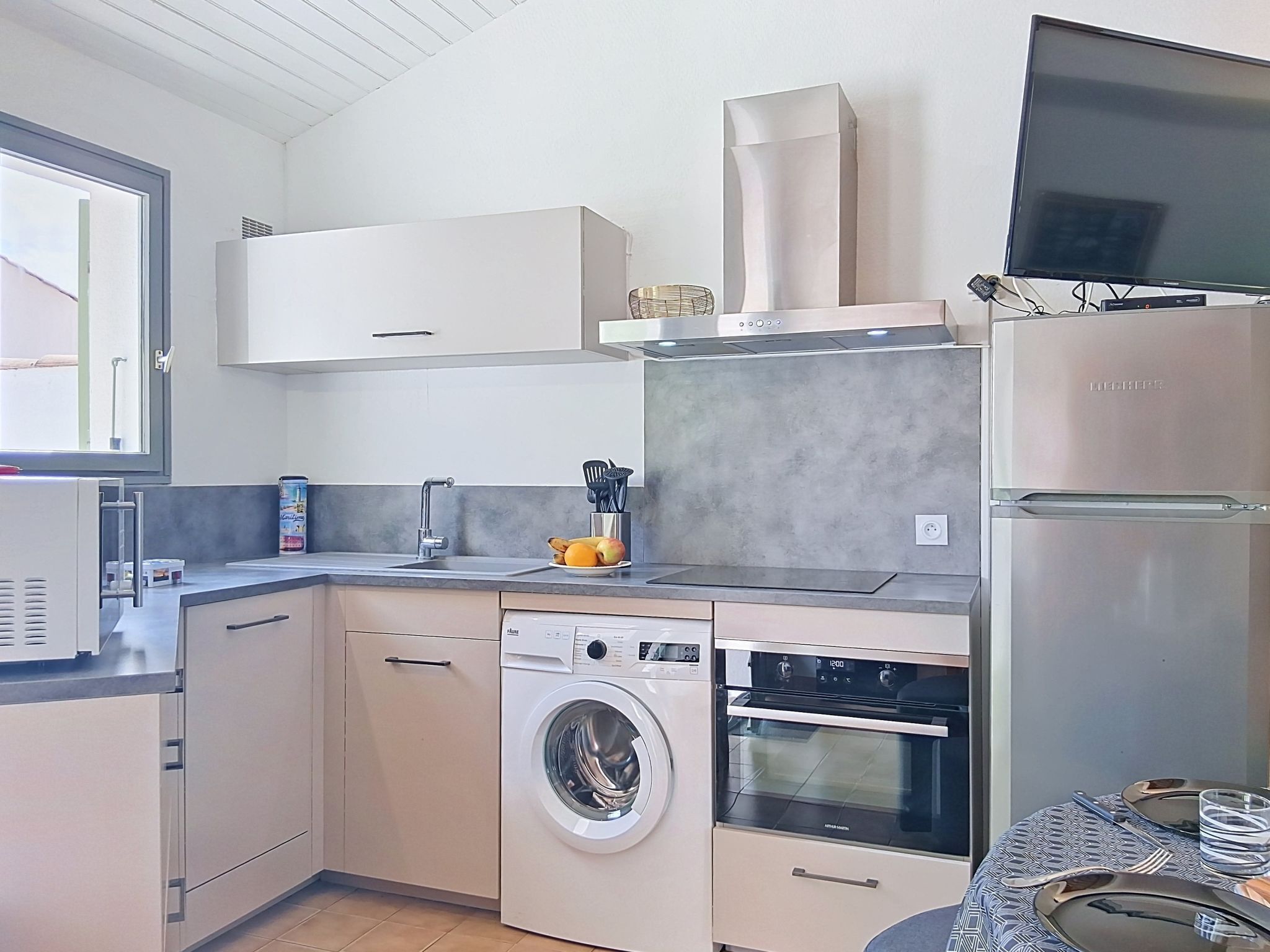 Een kleine keuken met een wasmachine, oven, magnetron en een flatscreen televisie.