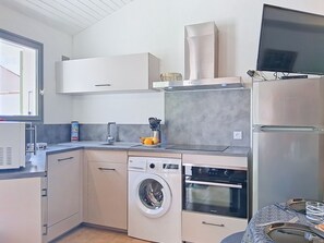 Eine kompakte Küche mit Waschmaschine, Backofen, Mikrowelle und einem Flachbildfernseher.